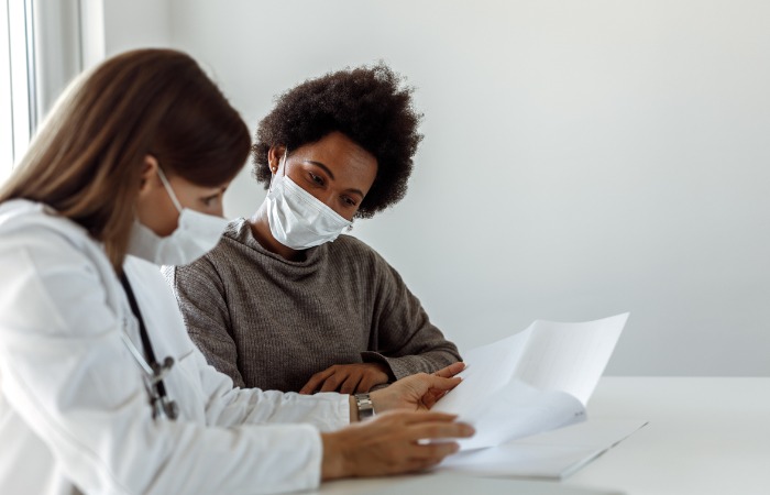 Masked doctor and patient discussing a document