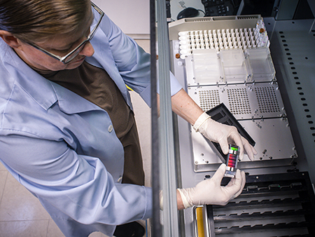 Shot from above, woman is working with sequencing slides in the Comprehensive Genomics Shared Facility cancer research laboratory directed by Dr. Michael Crowley, PhD (Associate Professor, Genetics Research; Co-Director, CGSF) and Dr. Shawn Levy, PhD (Adjunct Professor, Epidemiology; Co-Director, CGSF), 2019.