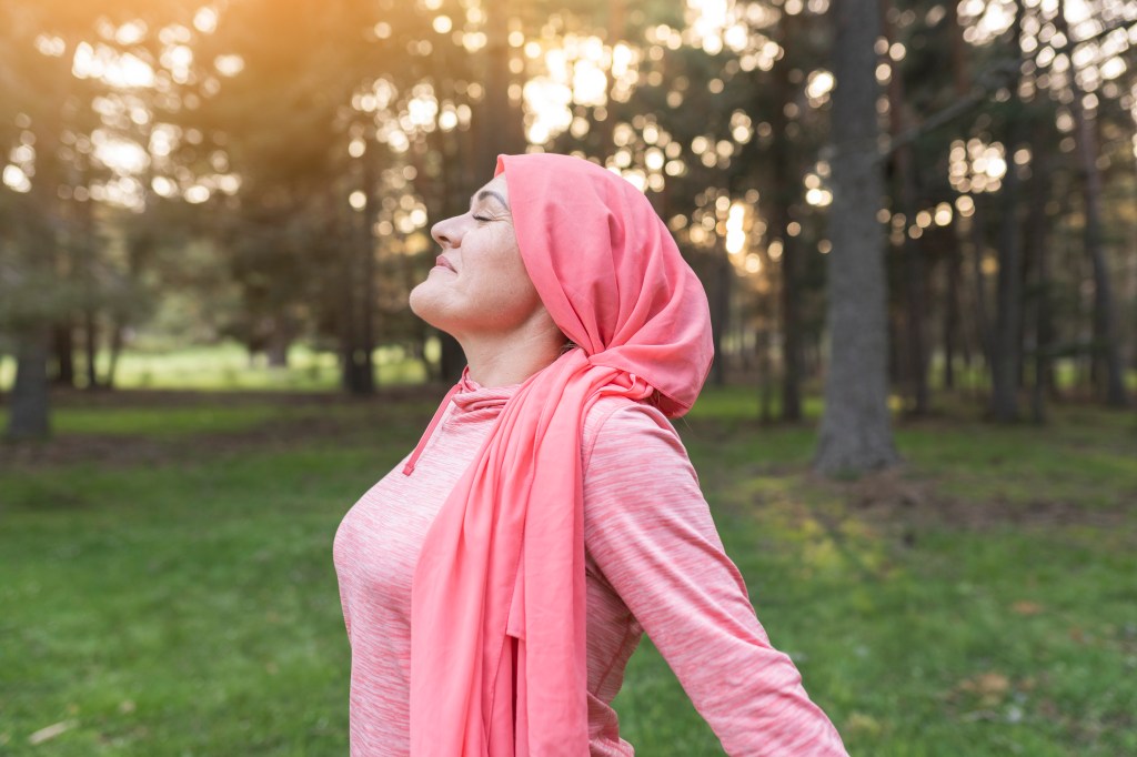 woman with cancer in nature while breathing fresh air, concept of a woman fighting cancer, woman with pink scarf relaxed.