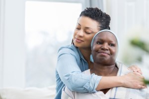 Caring adult daughter embraces her senior mother. The mid adult woman's eyes are closed.