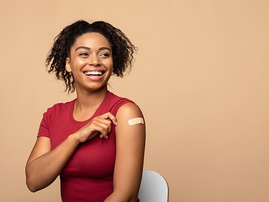 African American female sitting in a white chair smiling, wearing a red t-shirt and showcasing a bandaid on her arm