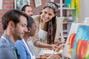Happy art instructor helps female student with painting