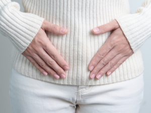 Woman in white sweater and pants placing hands over lower abdomen