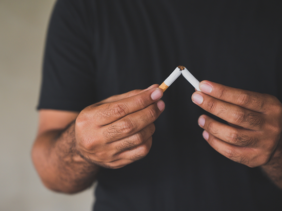 Man wearing a black t-shirt and breaking a cigarette in half with his hands