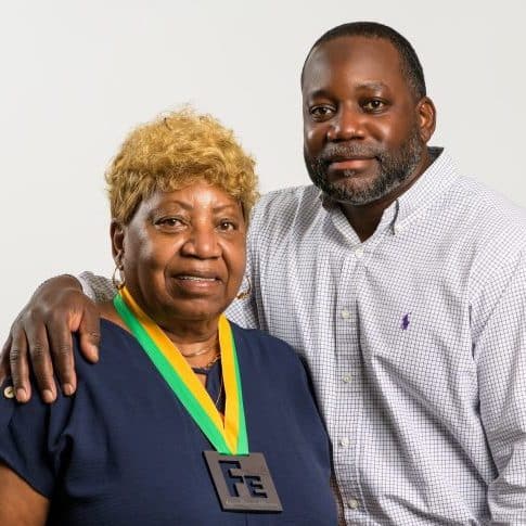 An older Black woman – Dorothy Brown –  in a navy blue dress with a medal reading "Fe," standing side-by-side with her son, Robert Brown.