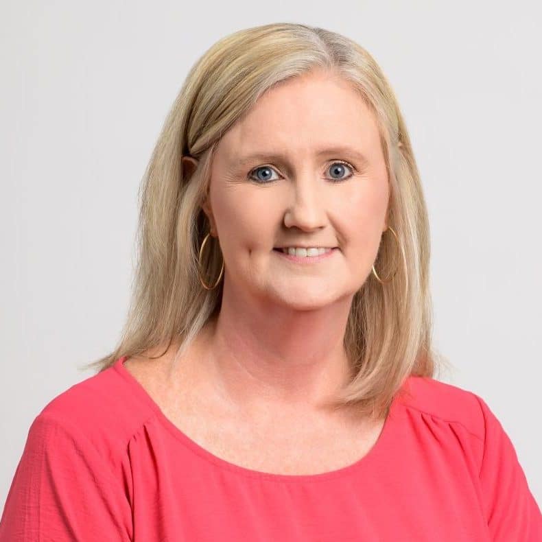 An adult woman – Dana Hanshaw – in a pink dress smiling directly at the camera.