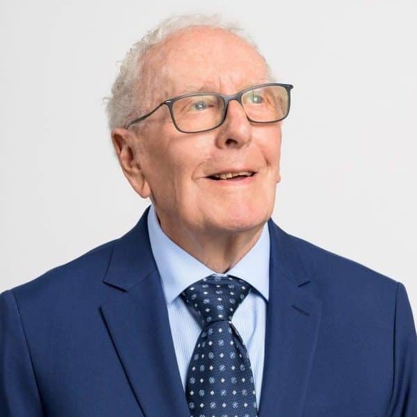 A photo of an elderly man – Michael Humphries – in a blue suit with glasses, smiling off-camera.