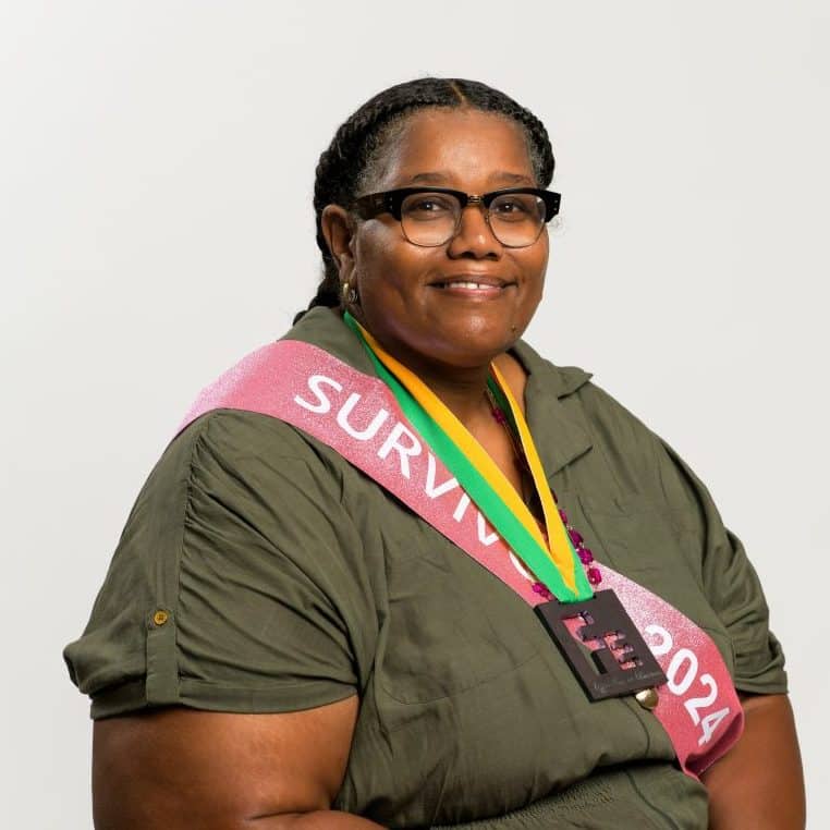 An adult Black woman – Tara Ransom – in a green dress, a pink sash reading "Survivor 2024," and an "Fe" Iron Strong medal.