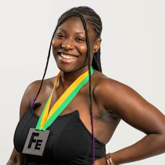A photo of a young Black woman – Iyanla Chaney – in a black dress wearing the "Fe" Iron Strong medal.