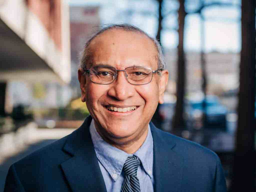 Anindya Dutta, MBBS, Ph.D.; a middle-aged doctor in a blue suit and matching blue tie stands outdoors. He wears glasses and smiles to camera. Behind him appears to be an outdoor part of the UAB campus.