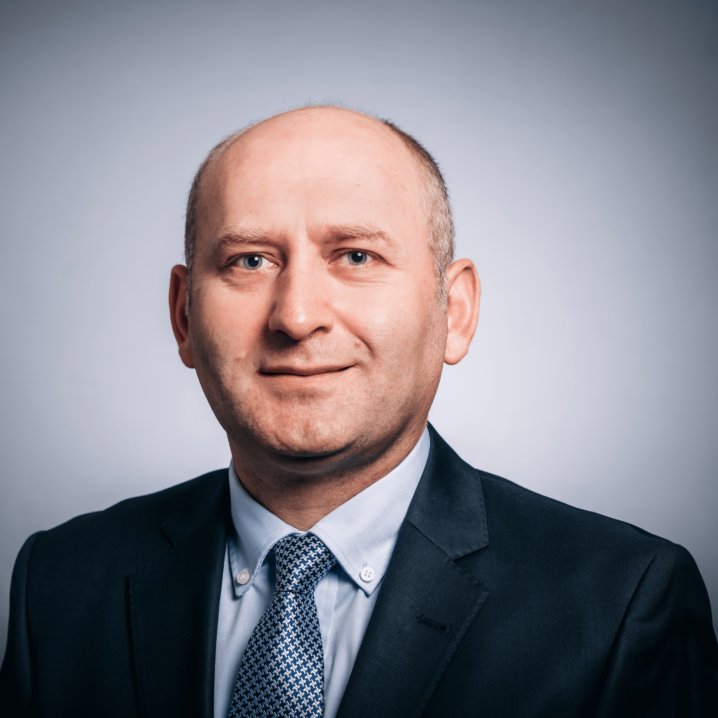 A headshot of a man with a shaved head in a dark suit with a pale tie - Mehmet Akce, M.D.