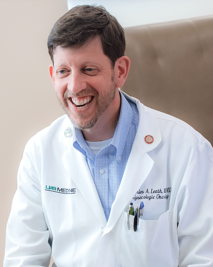 A photo of a doctor in a blue button-up shirt and a white lab-coat in clinic, talking to a patient; Charles Leath, M.D.