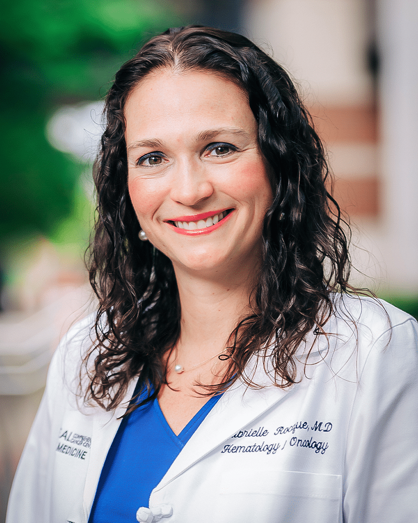 A photo of a scientist in a white labcoat and blue scrubs outside on the UAB campus; Gabrielle Rocque, M.D.