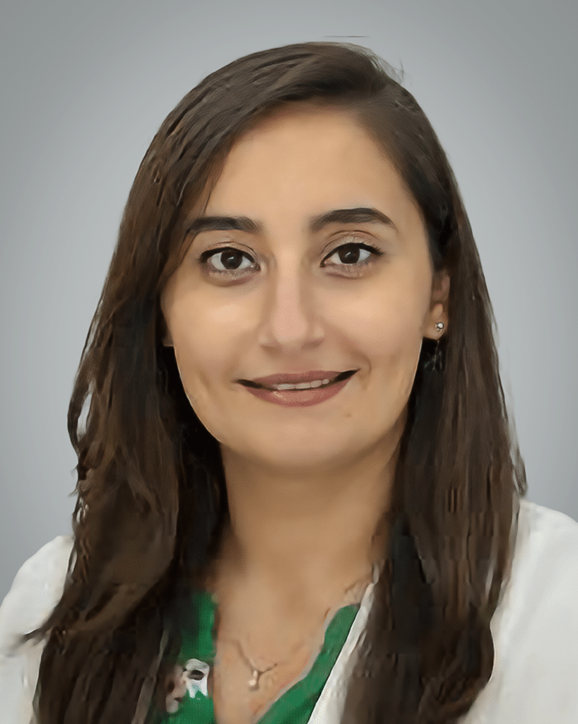 A headshot of a scientist in a white lab coat and a green shirt - Maya Khalil, M.D.