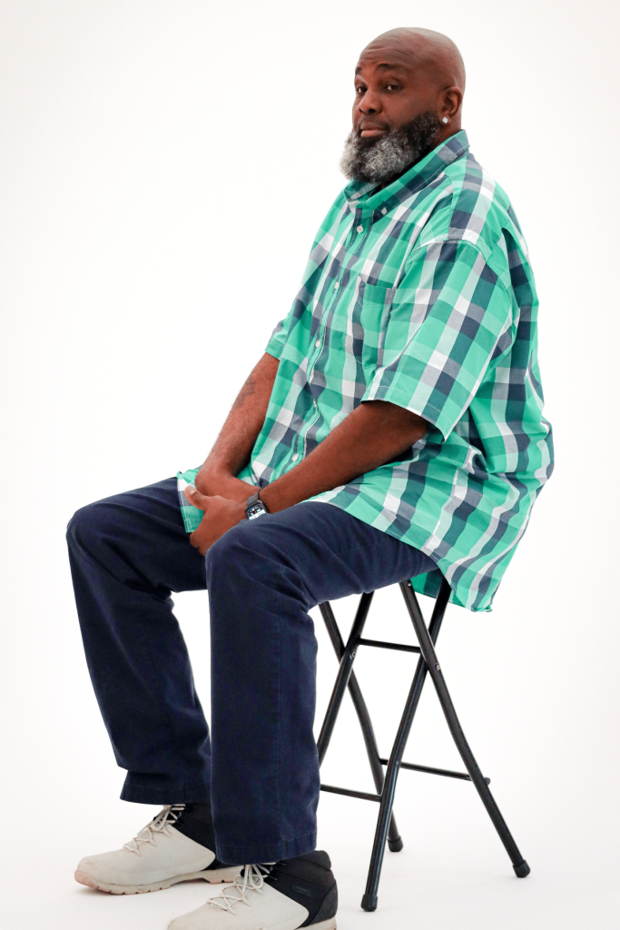 Iron Strong awardee Gregory Walker sitting on a chair against a white backdrop, having his photo taken.