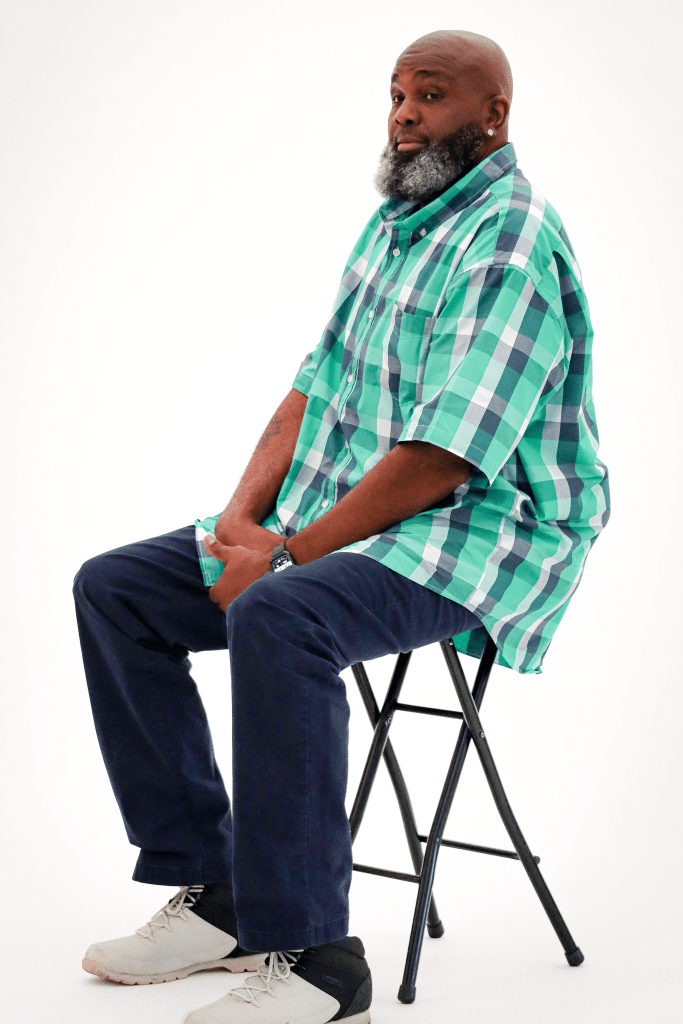 Iron Strong awardee Gregory Walker sitting on a chair against a white backdrop, having his photo taken.